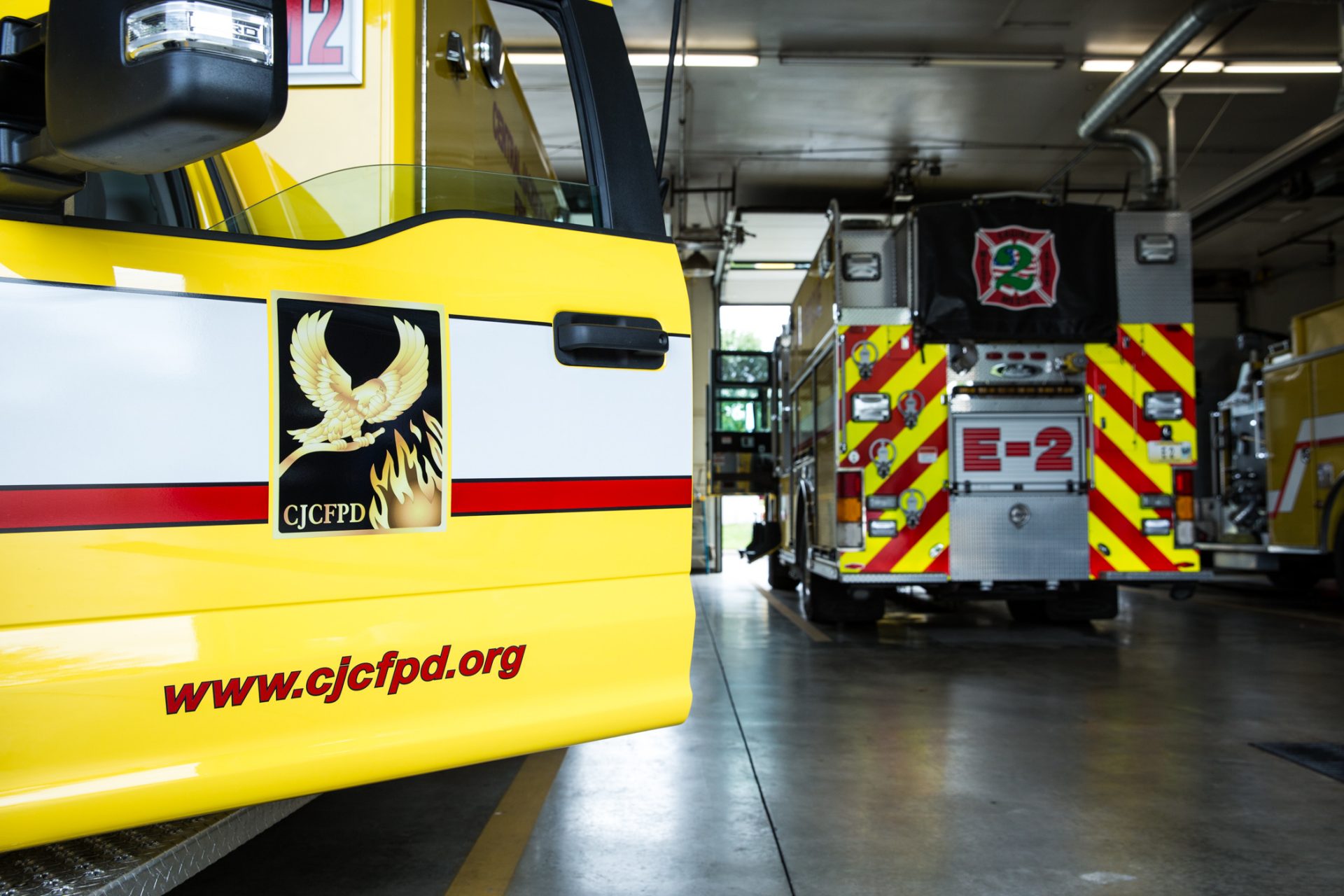 CJCFPD emergency vehicles parked inside a fire station bay, including a yellow truck and E-2 in the background.