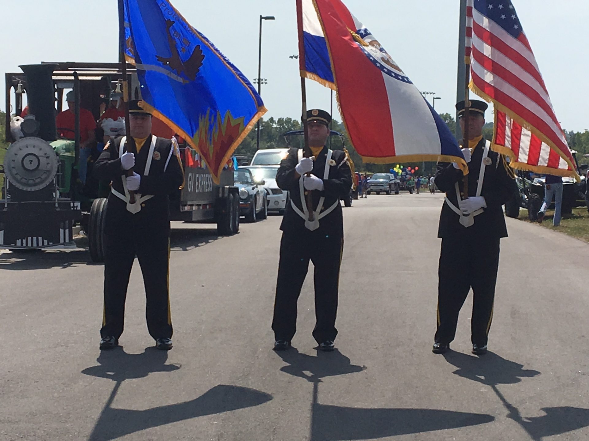 Honor guard members carry U.S. and department flags as they march down a roadway during a ceremony.