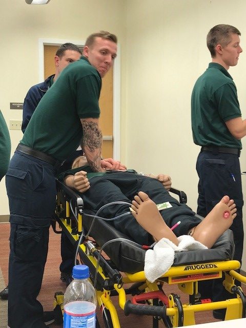 Students practice securing and moving a patient on a stretcher during EMS training.