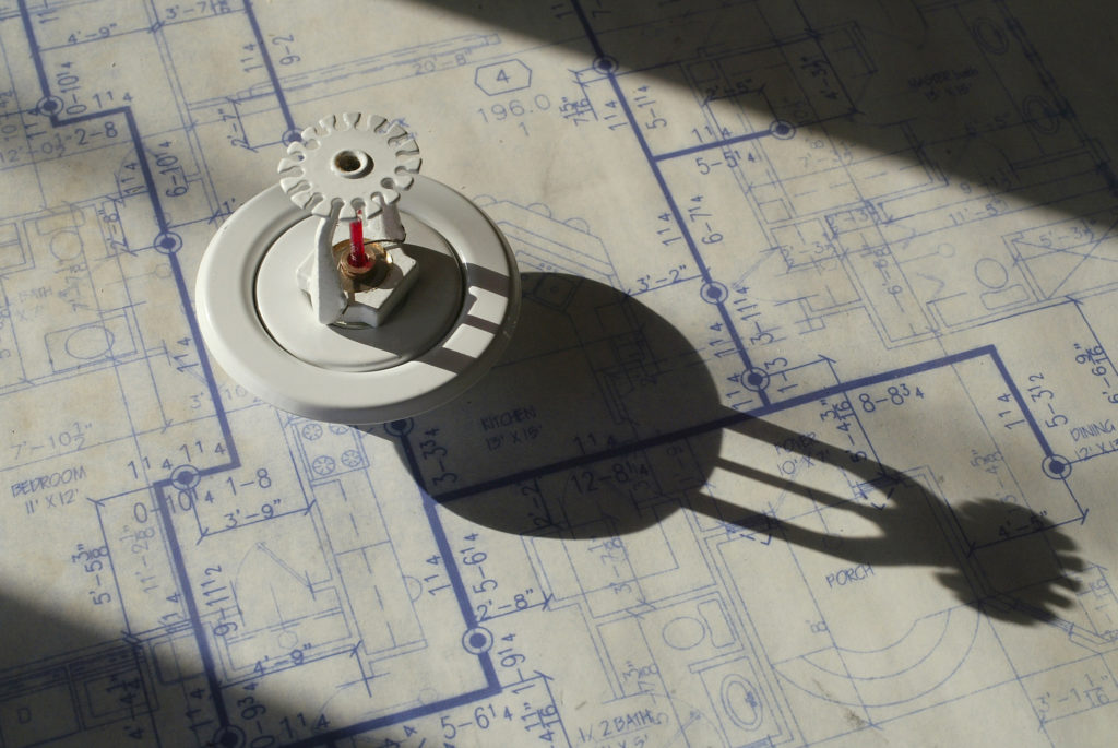 A fire sprinkler head resting on top of an architectural blueprint
