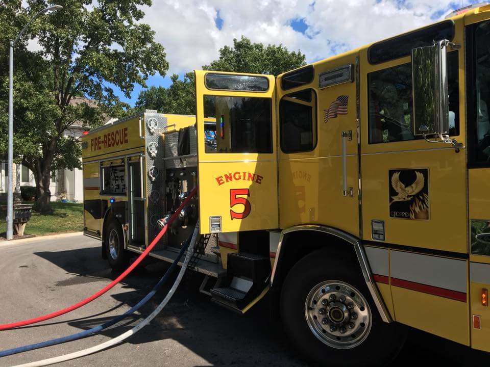 A yellow fire engine labeled Engine 5 is parked with hose lines stretched from the truck.